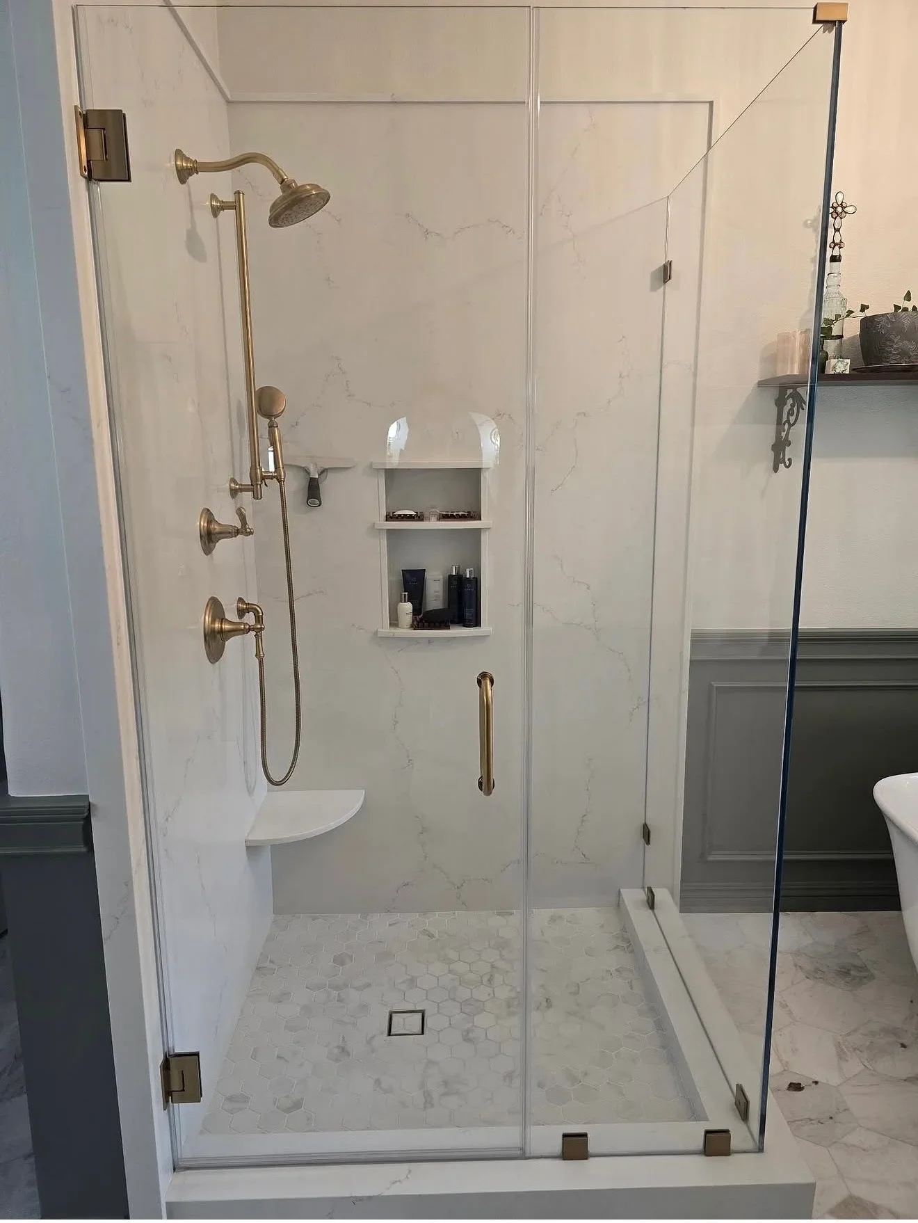 Frameless glass shower with marble tile walls, hexagonal floor mosaic, brushed brass fixtures and built-in niche