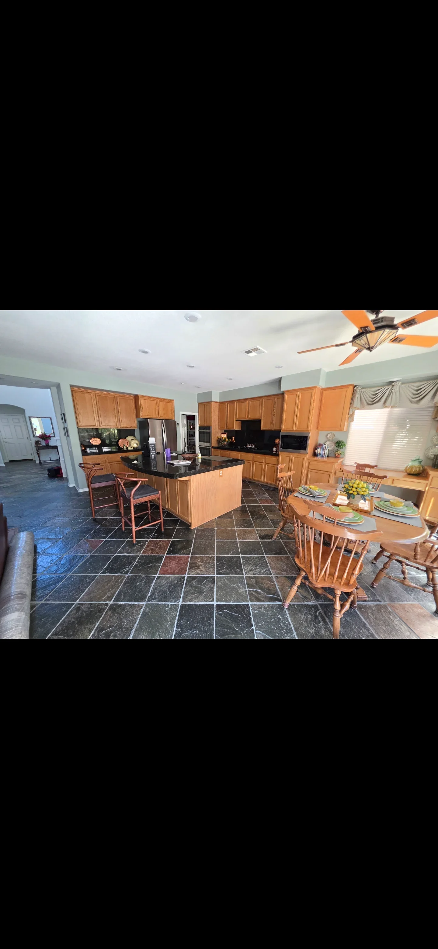 Kitchen with wood cabinets, black granite counters, slate tile floor, island, and dining area