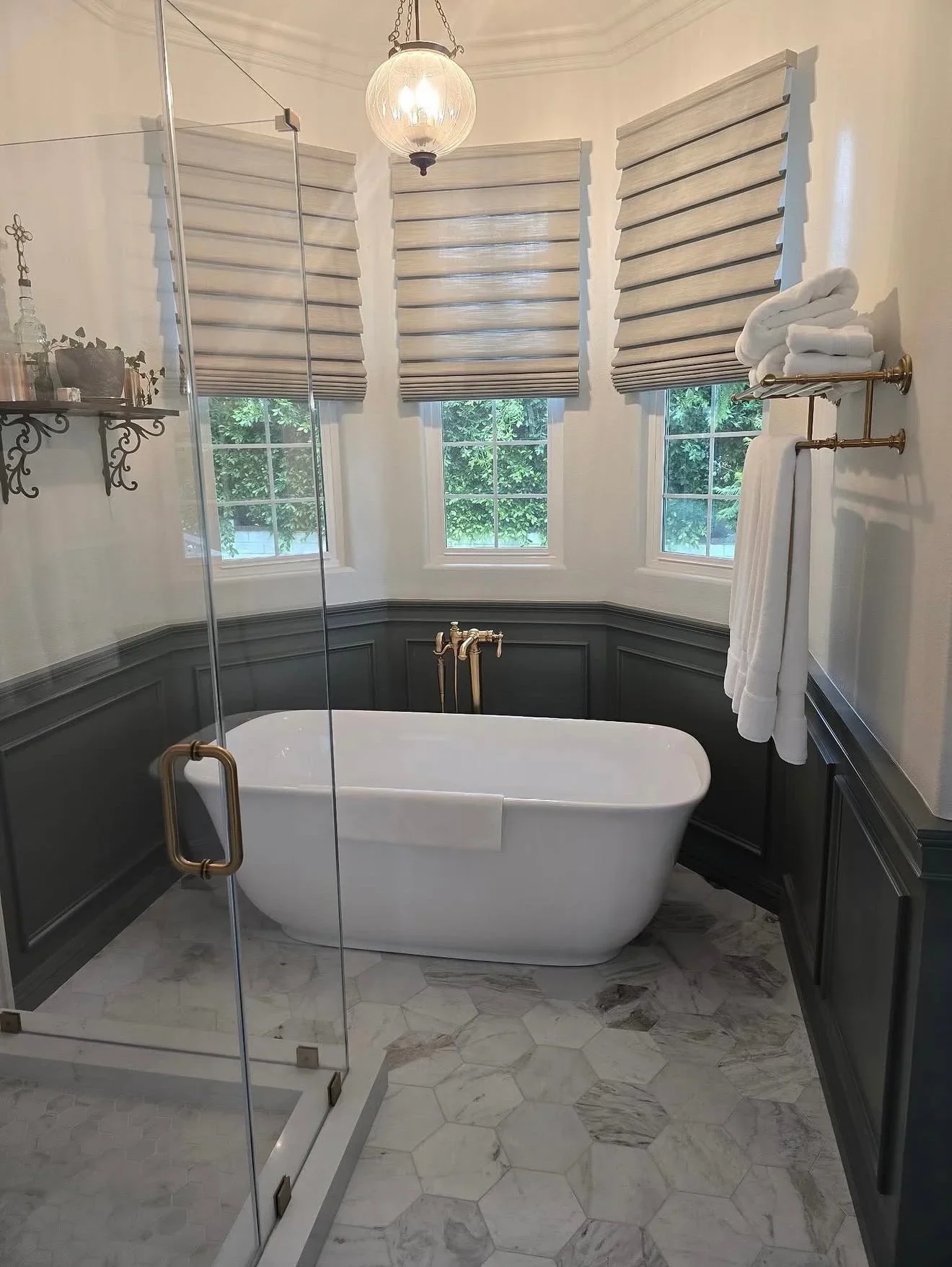 Freestanding white tub, marble hexagon floors, two-tone wainscoting, frameless glass shower, brass fixtures