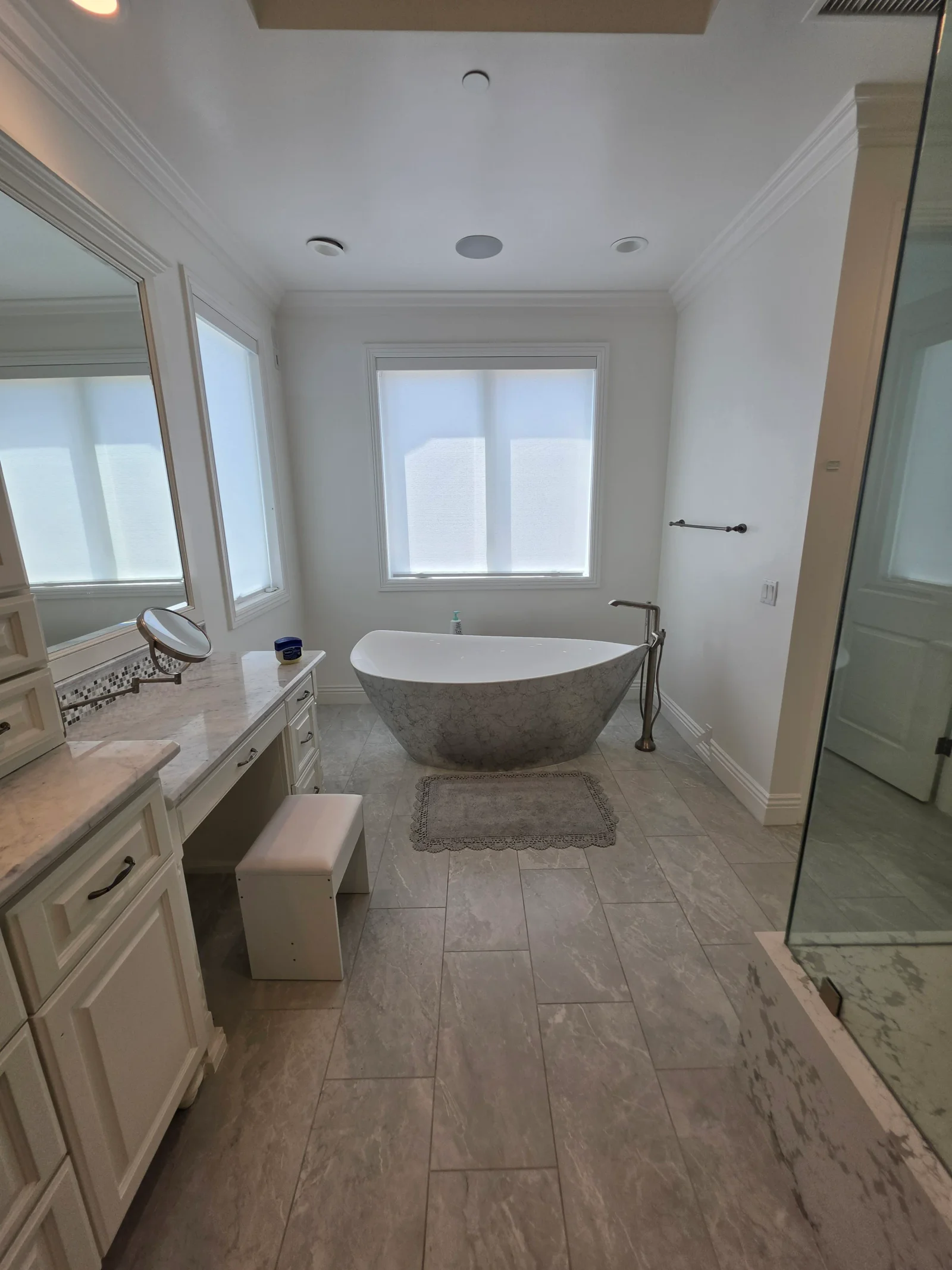 Master bathroom with stone soaking tub, white cabinetry, marble counters, and plank tile flooring