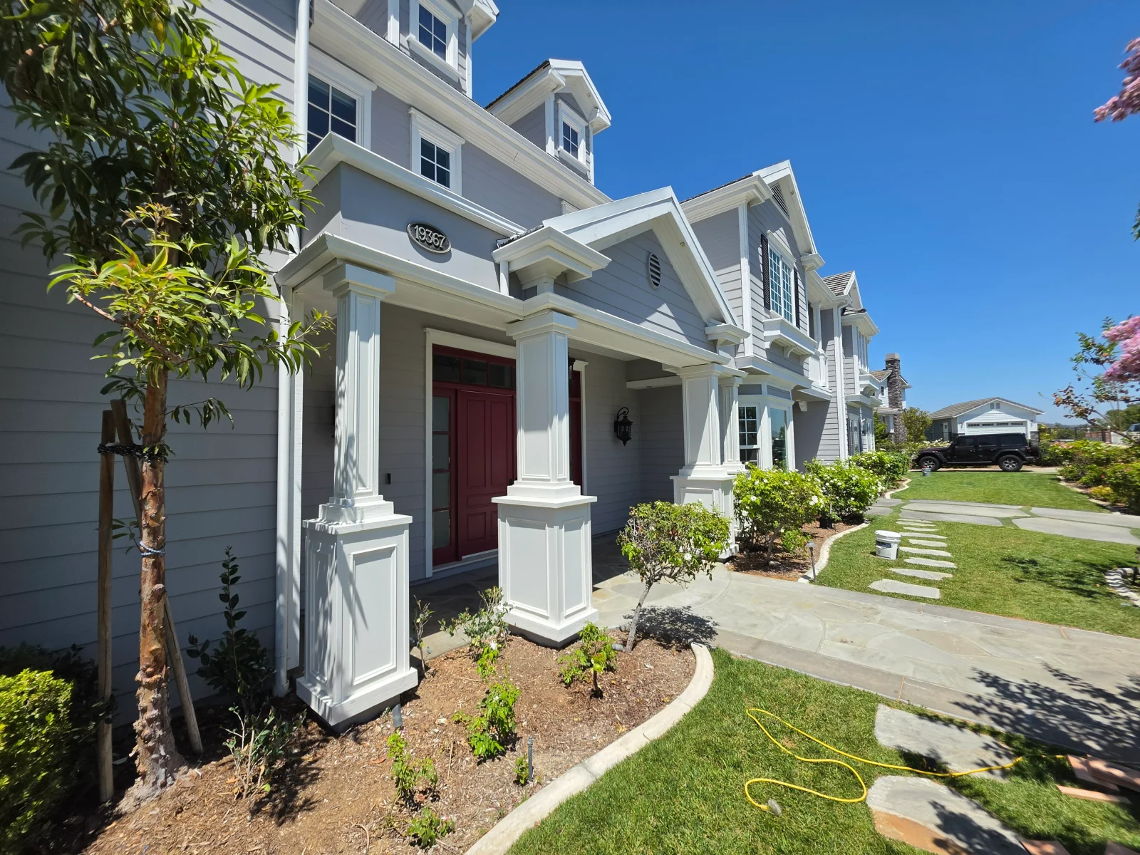 White farmhouse with new front porch, columns, burgundy door, and landscaping