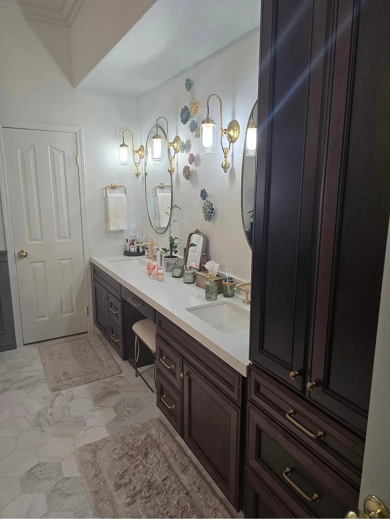Dark vanity with white quartz countertop, brass sconces, marble tile flooring, and dual mirrors in renovated bathroom