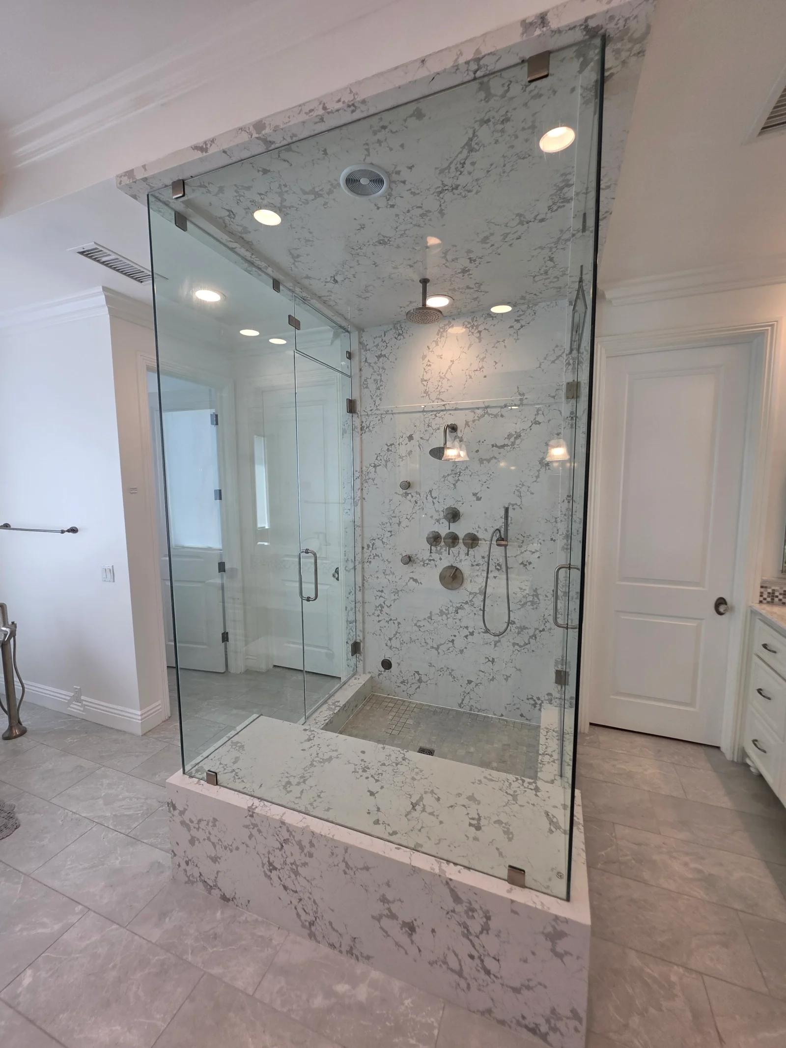 Frameless glass shower with marble tile walls, rainfall head, body jets, and recessed lighting